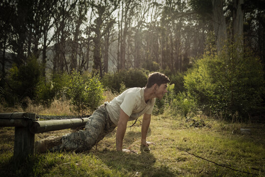 Fototapeta soldier doing incline push-up on grass with feet on wooden beam forest clearing, sunlight filtering