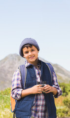 Middle Eastern boy standing on mountain path holding binoculars and wearing orange backpack