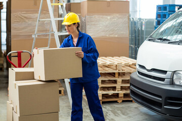 Cardboard boxes being loaded onto red pallet jack in warehouse with stacked pallets and white van