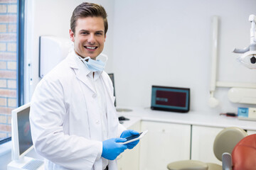 Male dentist examining tablet in dental treatment room with white coat and mask, copy space