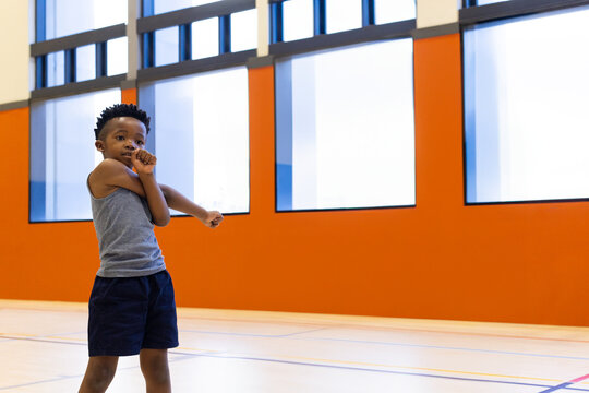 Fototapeta African-American schoolboy stretching arm across chest in gym with orange wall panels, copy space