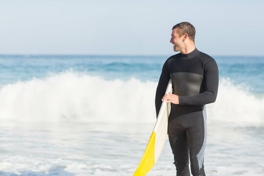 surfboard leaning on sandy beach near waves breaking on shoreline under blue sky