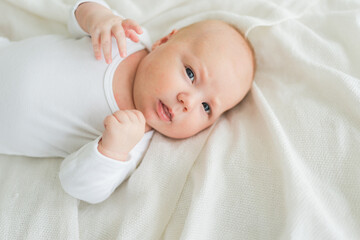 Happy baby. Cute little newborn girl with smiling face lying on bed in bedroom. Infant baby resting...