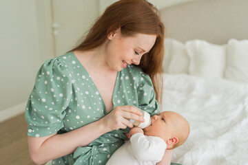Happy family at home. Mother holding little baby toddler child feeding milk from bottle. Newborn Infant baby girl sucking eating drinking milk. Mom of breast feeding baby. Motherhood happy child