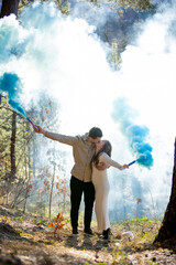 Cheerful joyfully celebrating their pregnancy couple surrounded by blue smoke in a beautiful, lush forest
