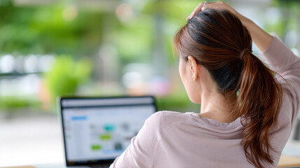 Fototapeta premium Woman with ponytail is sitting at desk, working on laptop in bright, modern office space. background is blurred, highlighting green, natural view outside