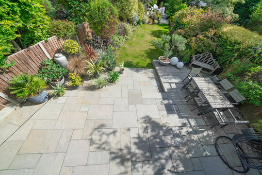 Aerial shot of beautiful English garden in spring with Indian sandstone patio and attractive shrubs and outdoor dining area.
