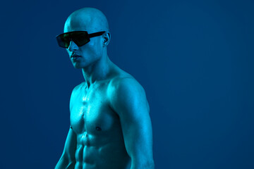 Athletic man with sunglasses posing against a vibrant blue background, showcasing strong physique...