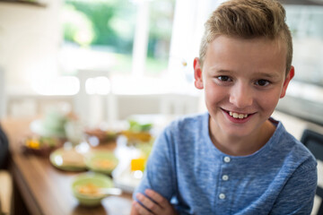 Boy wearing blue henley shirt smiling at wooden kitchen table with cereal, orange juice, copy space © wavebreak3