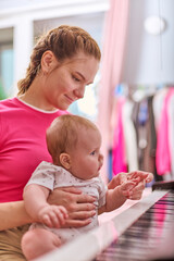 Young adult woman with tied-back hair and her baby girl engage with black and white synthesiser...