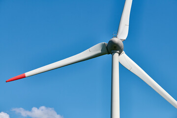 Detailed view of wind turbine with red tipped blades set against clear, vibrant blue sky on sunny...