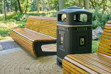 Wooden park bench beside litter bin on sunlit stone pathway in tranquil forest setting, inviting...