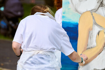 Young adult woman painting portrait outdoors, in urban park. Focus on her artistic process with...