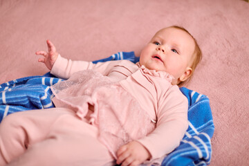 Young caucasian female infant with light hair lies on blue blanket. Soft pink outfit contrasts with vibrant background. Calm emotion under gentle indoor lighting