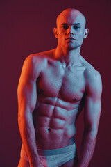Athletic man posing confidently against a dramatic colored background, showcasing strong physique and toned muscles. The image reflects a blend of artistic lighting.