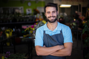 Man standing with crossed arms by wooden display tables in flower shop arranging colorful bouquets