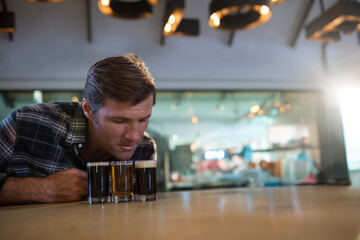 Man leaning over bar counter in brewery taproom inspecting beer flight under warm lights