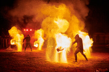Silhouette of two fire performers with sparkling fire staff erupting in night sky, showcasing energy and artistry of fire manipulation during an outdoor fire show