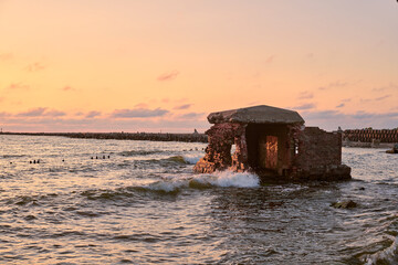 Weathered fortress remnants stand resilient on baltic sea coast, bathed in serene sunset hues,...