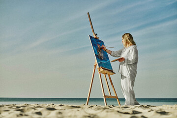 Young woman artist stands near ocean, painting on easel. Serene beach environment complements her...
