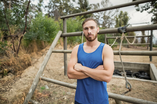 Fit man in sportswear on training field facing obstacle course with hanging ropes and tire pit