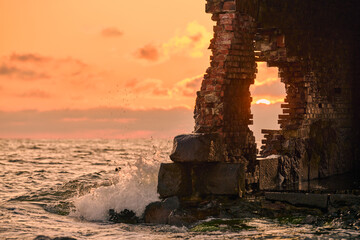 Weathered brick structure by sea at sunset evokes history and change. Waves crash against ancient...