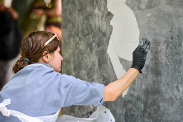 Young white female artist applying chalk on large vertical canvas. Engaged, focused expression....