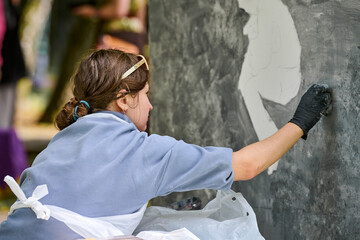 Young white female artist applying chalk on large vertical canvas. Engaged, focused expression....