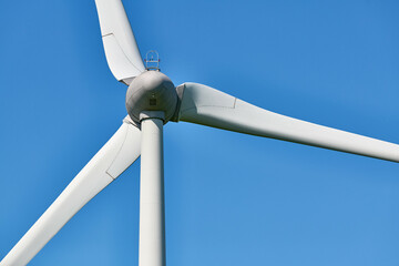 Detailed view of wind turbine with red tipped blades set against clear, vibrant blue sky on sunny day, evoking clarity and commitment to environmental sustainability