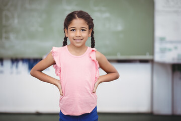 Preteen girl standing with hands on hips and smiling in classroom with chalkboard equations
