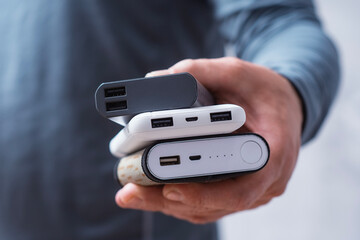 Man hand holds three different power bank. Modern portable chargers with USB connectors for charging smartphones and gadgets.