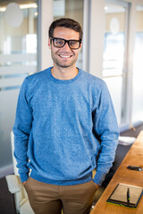 Male office worker standing in office wearing blue sweater near digital tablet and glass partition