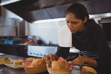 Indian woman chef adding rolls into baskets beside sandwiches on counter in kitchen, copy space