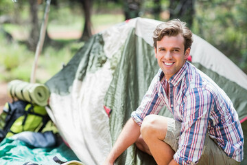 Man kneeling and assembling dome tent on tarp in woods with backpack, roll-up pad, copy space