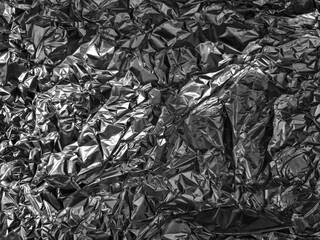 Crinkled metallic surface with irregular, shiny textures creating abstract shapes and patterns. The play of light and shadow enhances the three-dimensional appearance