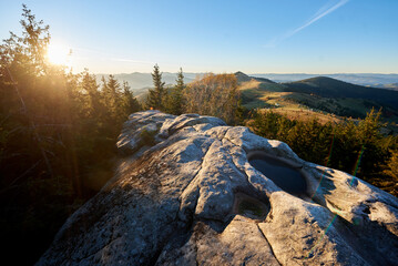 Scenic sunrise at Pysanyi Kamin in Carpathians, Ukraine. Rocky surface in foreground. Breathtaking view of rolling hills, dense forests, and distant mountains illuminated by soft morning light.