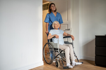 Young female nurse carrying a wheelchair with an elderly woman