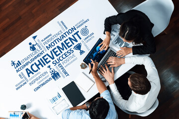 Aerial view of a diverse team collaborating over a table, surrounded by words symbolizing achievement, motivation, and success, emphasizing growth and strategic planning. Amity