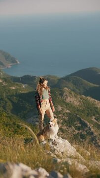 Happy, joyful young girl stands in the mountains with her border collie dog, the bay and mountains are visible against the background. Pet and his owner