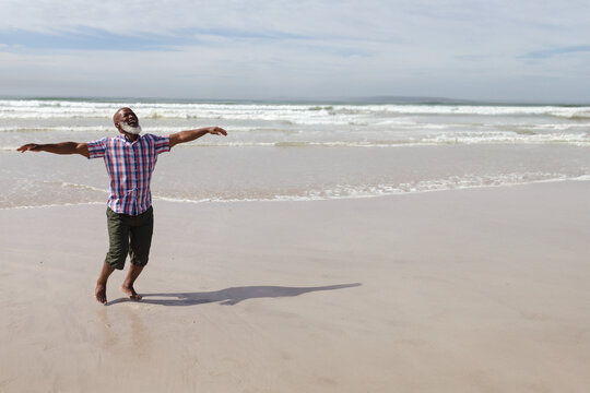 African American man stretching arms on beach wearing rolled-up pants barefoot with waves rolling