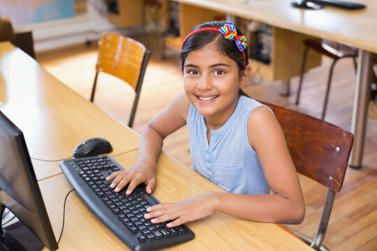 Indian child wearing rainbow bow headband typing on keyboard at computer lab desk with world map