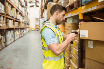 Male worker wearing safety vest using scanner scanning barcodes on boxes in warehouse, copy space