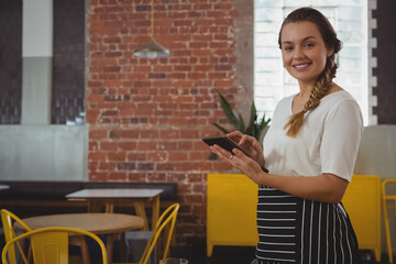 Female server wearing striped apron holding tablet in cafe near brick wall and tables, copy space