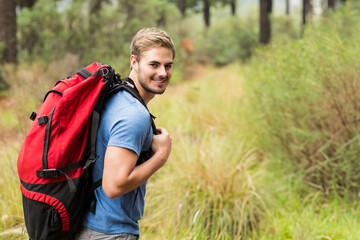 Fototapeta premium Male hiker hiking on pine forest trail smiling, carrying red backpack with black straps, copy space