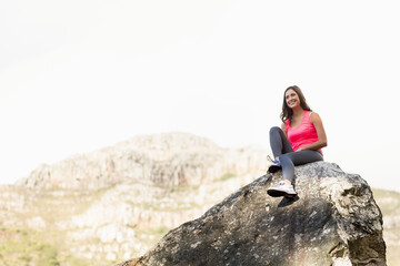 Naklejka premium Woman sitting on boulder in mountains wearing athletic shoes, leggings, pink tank top, copy space