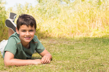 Child boy lying on stomach in sunny open meadow surrounded by tall grass, copy space