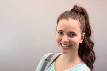 Female student standing in hallway wearing mint green top and gray backpack strap, copy space