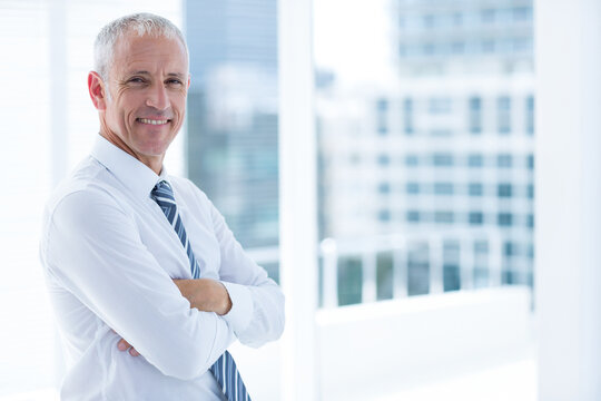 Middle-aged man in suit standing by floor-to-ceiling windows overlooking city skyline, copy space