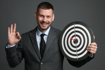 Targeting. Man with dart board and arrow showing ok gesture on grey background