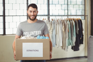 Male volunteer standing in sorting room holding donation box near clothing rack and grid windows